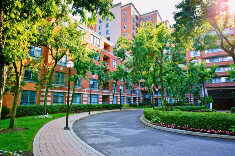 Brick condominium building with tree-lined walkways and a landscaped drive, illustrating what condo insurance covers