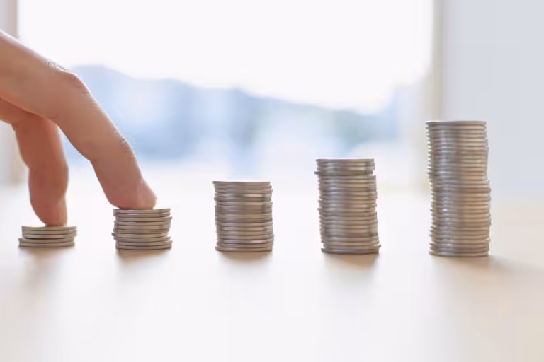 Fingers stepping up rising stacks of coins, illustrating how inflation affects insurance rates