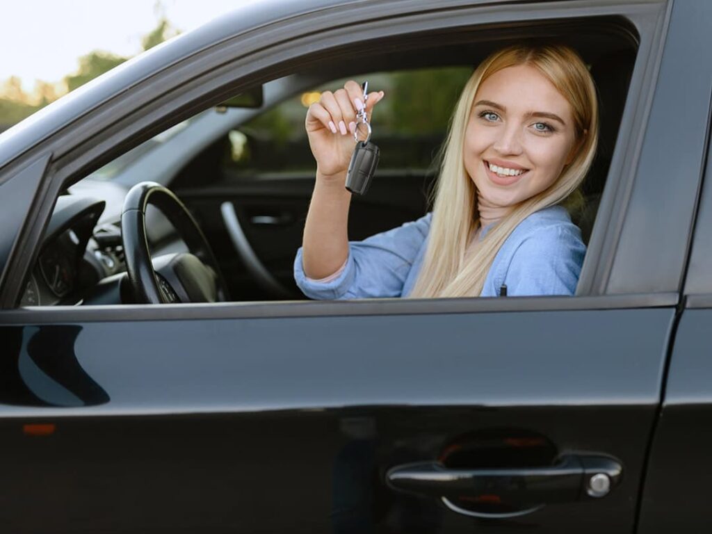 A blond girl in a black card holding up keys and smiling